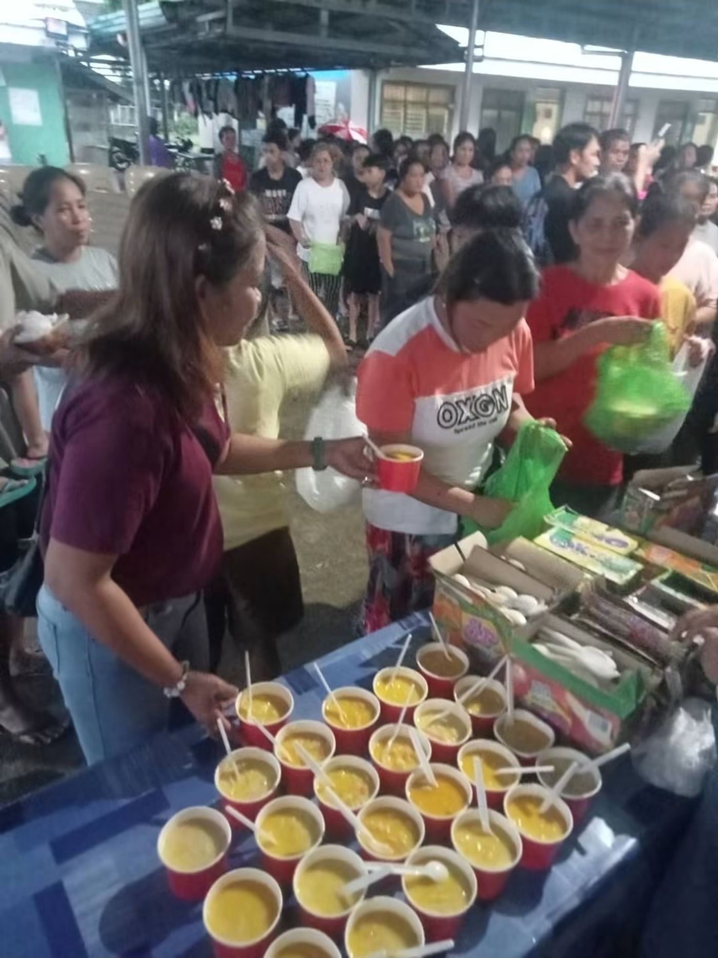 Volunteers passing cups of hot food across a table to people waiting
