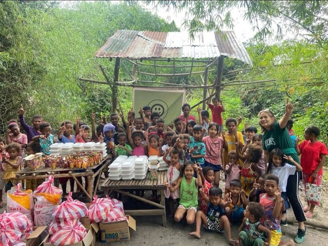 Children gathered around tables of food packages at a Charity Good distribution, beneath the Charity Good banner